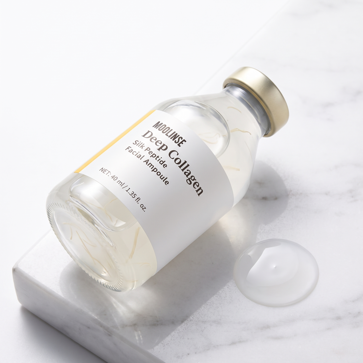MOOLINSE Deep Collagen Silk Peptide Facial Ampoule bottle with gold cap on white marble, showing the pale serum with fine silk peptide strands